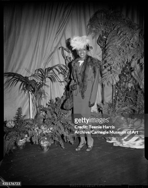 Gloria Golden Grate modeling suit, fur stole, and feathered hat, on stage with potted plants for sixth annual Beauty Shop Owners Fashion Show,...