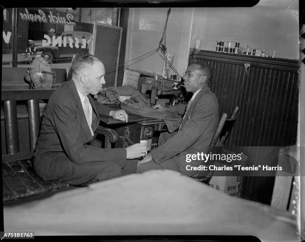 Attorney Theron B Hamilton and tailor Clark Watts seated in front of sewing machine in Watt's Brothers Cleaner Shop , Hill District, Pittsburgh,...