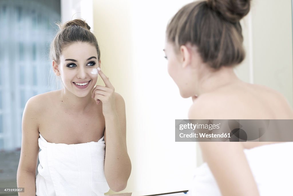 Portrait of teenage girl putting on some lotion while looking at her mirror image