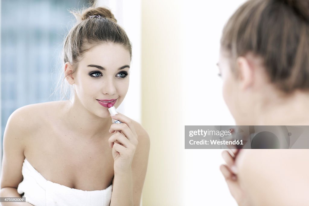 Portrait of teenage girl putting lipstick on while looking at her mirror image