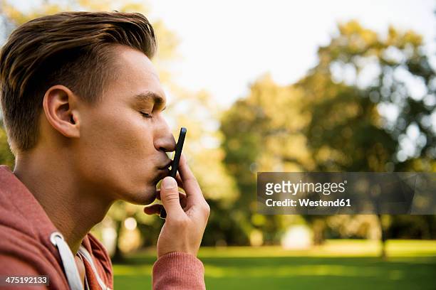 young man kissing his smart phone, close-up - tomber amoureux photos et images de collection