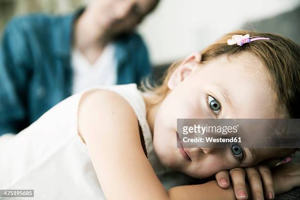 thoughtful little girl lying on sofa, her father standing in the background - lying on front stock pictures, royalty-free photos & images