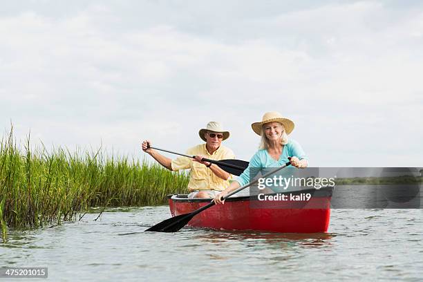 senior couple sitting in canoe, paddling with oars - seniors canoeing stock pictures, royalty-free photos & images