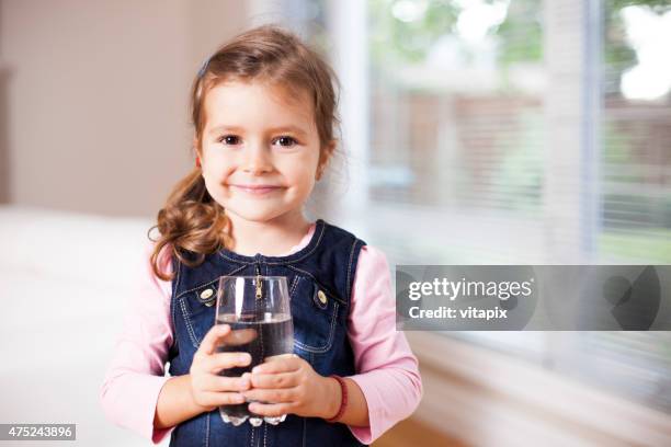 niña sosteniendo un vaso de agua, mirando a la cámara - niño-tomando-agua fotografías e imágenes de stock