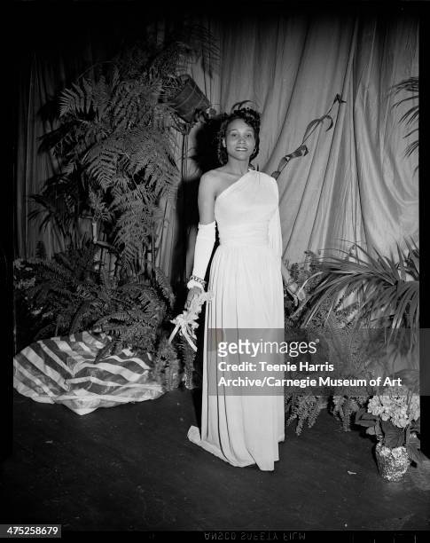 Leanora Worthington modeling long gown with single shoulder, detached sleeve, and chain bracelet, on stage with potted plants for sixth annual Beauty...