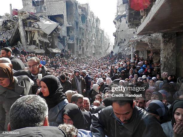 In this handout provided by the United Nation Relief and Works Agency , Residents wait in line to receive food aid distributed in the Yarmouk refugee...