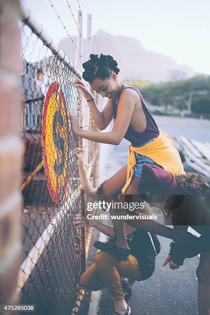 amigos ajudando afro grunge urbano menina escalada vedação - violar propriedade alheia imagens e fotografias de stock