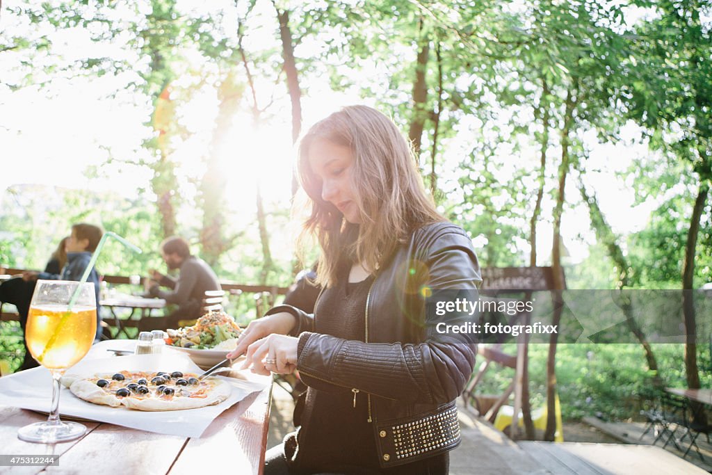 Junge Frau schneiden Sie pizza im Biergarten
