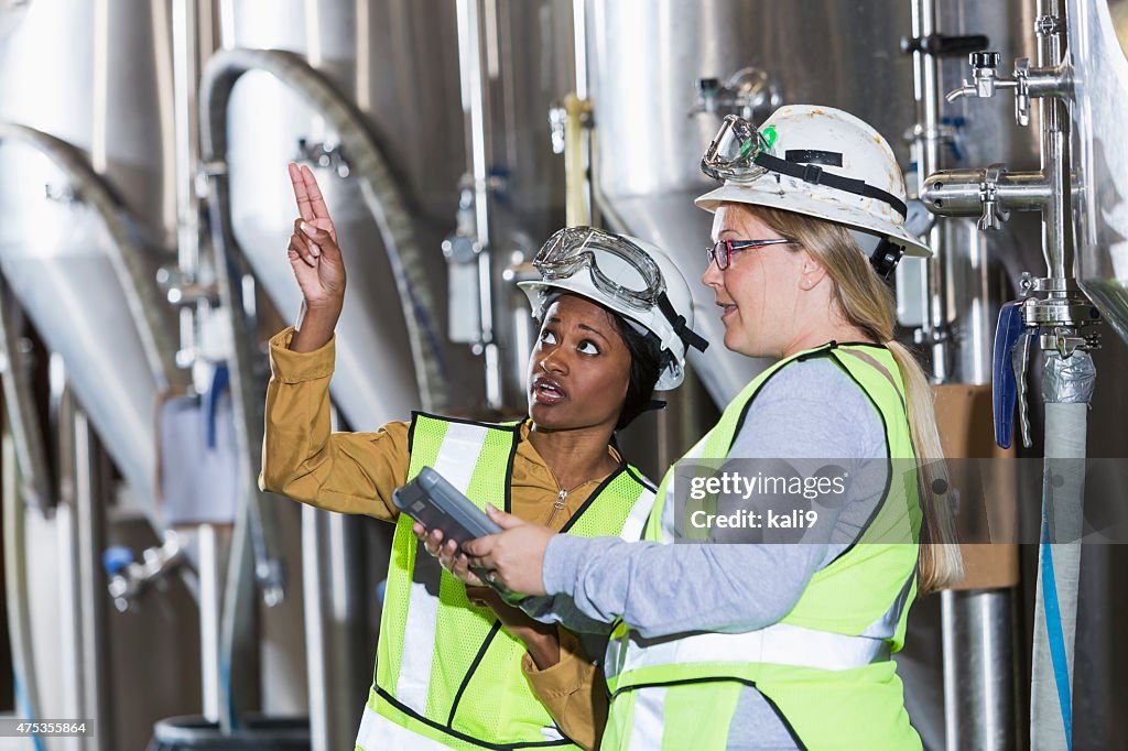 Two women working in a factory wearing hardhats