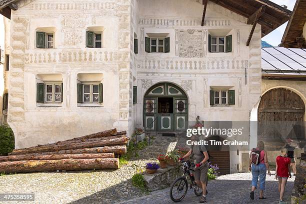 Tourists pass Pension Val Tuoi in the Engadine Valley in village of Guarda with painted stone 17th Century houses, Switzerland