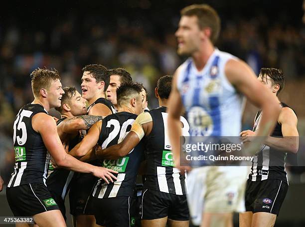 Jamie Elliott of the Magpies is congratulated by team mates after kicking a goal whilst Lachlan Hansen of the Kangaroos looks dejected during the...