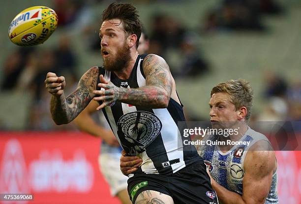 Dane Swan of the Magpies handballs whilst being tackled by Jack Ziebell of the Kangaroos during the round nine AFL match between the Collingwood...