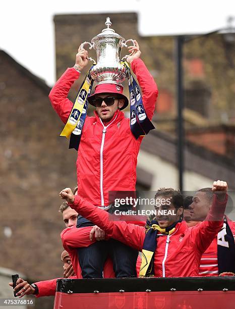 Arsenal's English midfielder Jack Wilshere holds the trophy as he stands alongside Arsenal's French midfielder Mathieu Flamini and teammates on the...