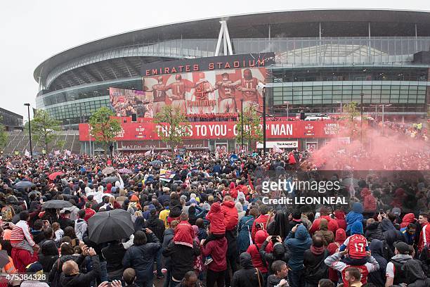 Fans watch in the rain as Arsenal players celebrate with the trophy outside the Emirates Stadium during the Arsenal victory parade in London on May...