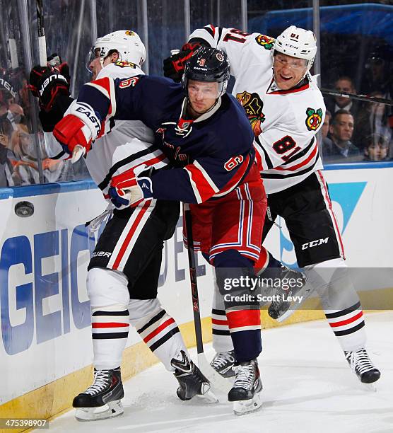 Anton Stralman of the New York Rangers battles for the puck along the boards against Patrick Sharp and Marian Hossa of the Chicago Blackhawks at...