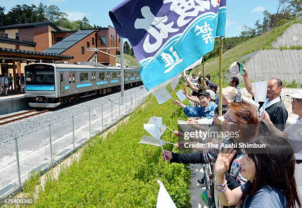 Local residents welcome the train service resumption by waving flags on May 30, 2015 in Higashimatsushima, Miyagi, Japan. After a more than four-year...