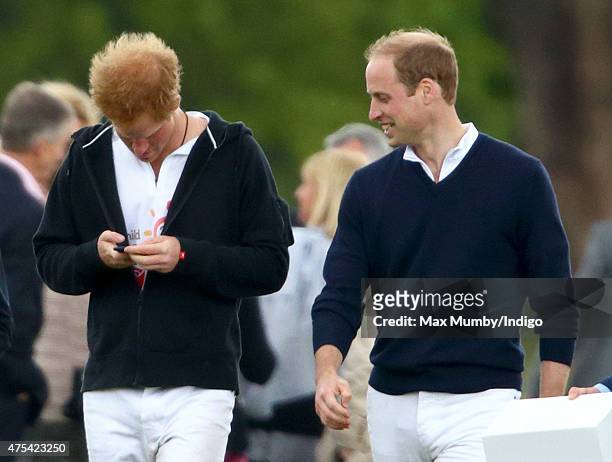 Prince William, Duke of Cambridge looks on as Prince Harry uses his mobile phone on day 2 of the Audi Polo Challenge at Coworth Park on May 31, 2015...