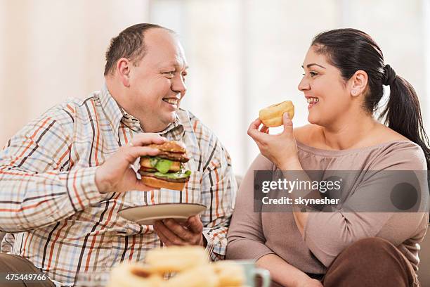 sorridente coppia di mangiare cibo malsano grasso a casa. - fat people eating donuts foto e immagini stock