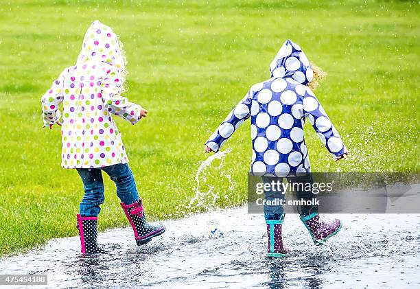 two young girls splashing through puddle in the rain - regnkläder bildbanksfoton och bilder