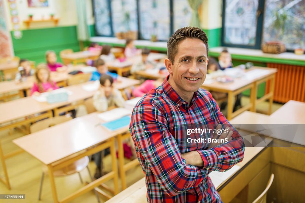 Happy elementary school teacher with crossed arms in the classroom.