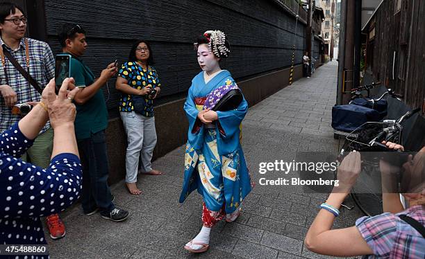 Tourists take photographs of a maiko, or apprentice geisha, walking through the Gion area of Kyoto, Japan, on Thursday, May 28, 2015. Spending by...