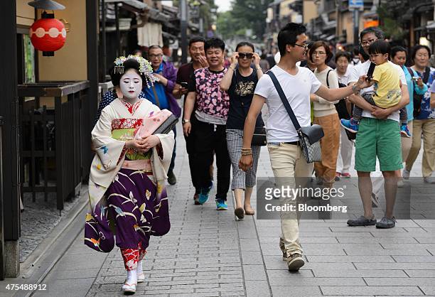 Tourists look on as a maiko, or apprentice geisha, left, walks past in the Gion area of Kyoto, Japan, on Thursday, May 28, 2015. Spending by visitors...