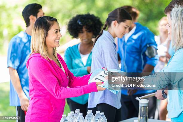 young woman receiving number and t-shirt after registering for race - register bildbanksfoton och bilder
