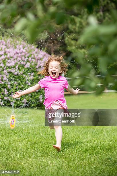 little girl with curly red hair running through sprinkler - ginger bush stock pictures, royalty-free photos & images
