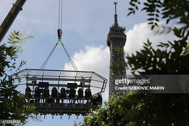 The Eiffel Tower is seen in the background as people sit around a table suspended 30 meters above the ground and watch Roland Garros 2015 French...