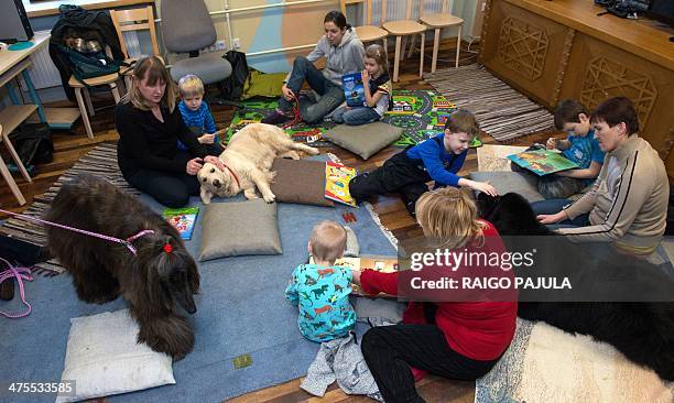 Children read to a dog hired by a library on February 26, 2014 in Tartu, south Estonia to encourage kids to practice reading books aloud, to increase...