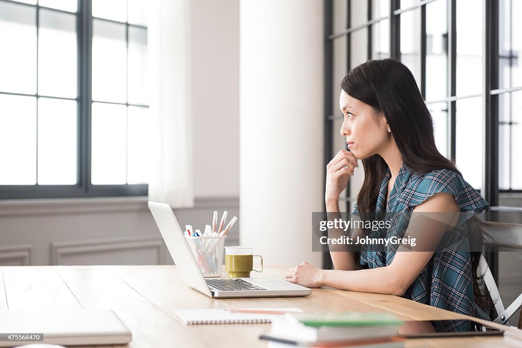 Thoughtful young Asian woman at work