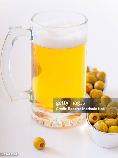 Mug of frothy beer and green olives for snack, a mug of beer beside a dish of green olives.