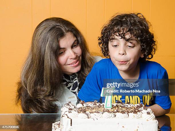 Latino boy with mother blowing candle on cake, celebrating his seventh birthday.