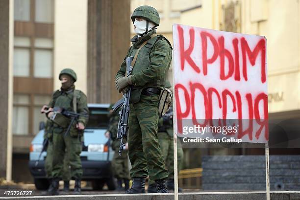 Heavily-armed soldiers without identifying insignia guard the Crimean parliament building next to a sign that reads: "Crimea Russia" after taking up...