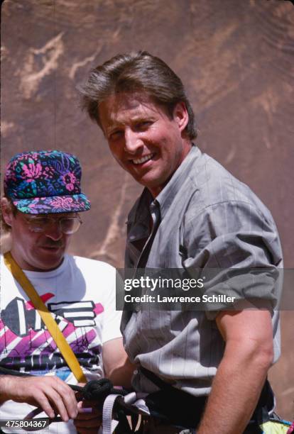 American actor Bruce Boxleitner is hooked into a harness by an unidentified crewmember in preparation for a rock climbing scene in the tv movie...