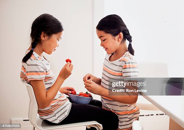 young twins in striped shirts sharing strawberries - identical twin stock pictures, royalty-free photos & images