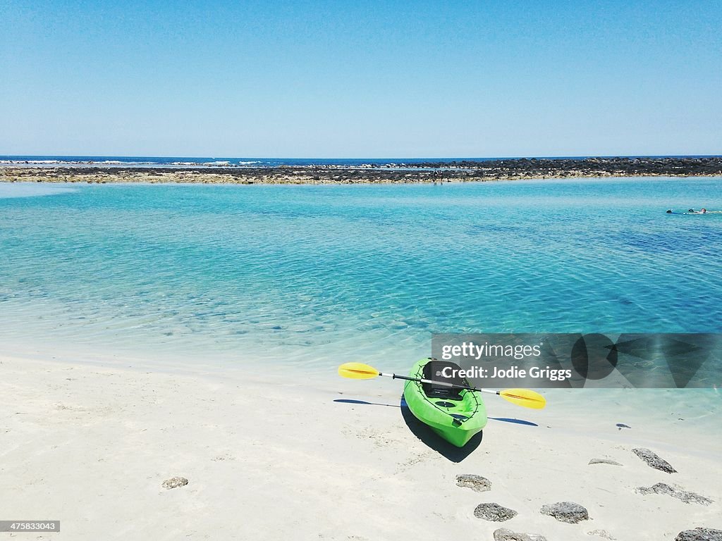Empty green kayak on sand at secluded beach