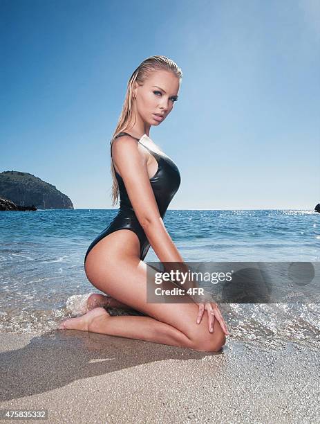 beautiful blond woman in a black latex swimsuit, pin-up pose - sekssymbool stockfoto's en -beelden