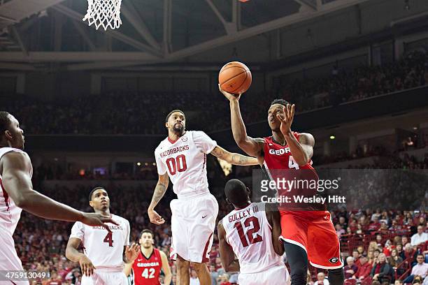 Charles Mann of the Georgia Bulldogs goes up for a shot against Fred Gulley III and Rashad Madden of the Arkansas Razorbacks at Bud Walton Arena on...