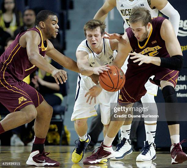 Spike Albrecht of the Michigan Wolverines tries to steal the ball from Andre Hollins, left, and Elliott Eliason of the Minnesota Golden Gophers...