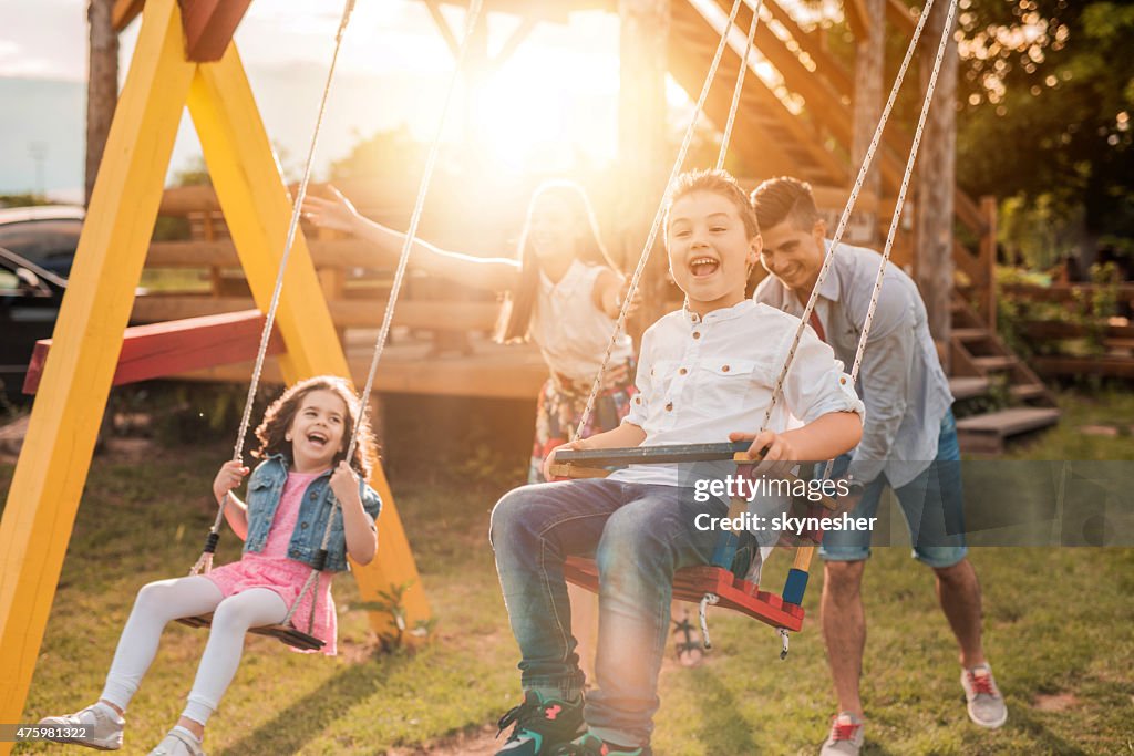 Happy young parents swinging their children at sunset.