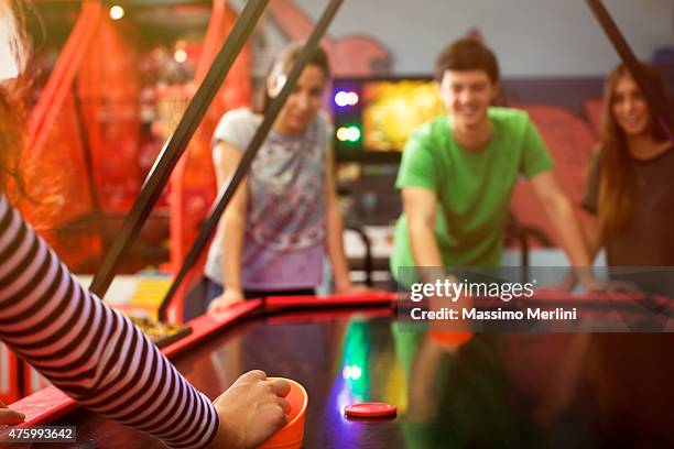 vier freunde, spaß haben und spielen air-hockey-spiel - amusement arcade stock-fotos und bilder