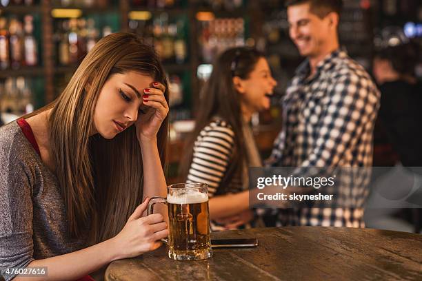 sad young woman in bar with happy couple in background. - envy stock pictures, royalty-free photos & images