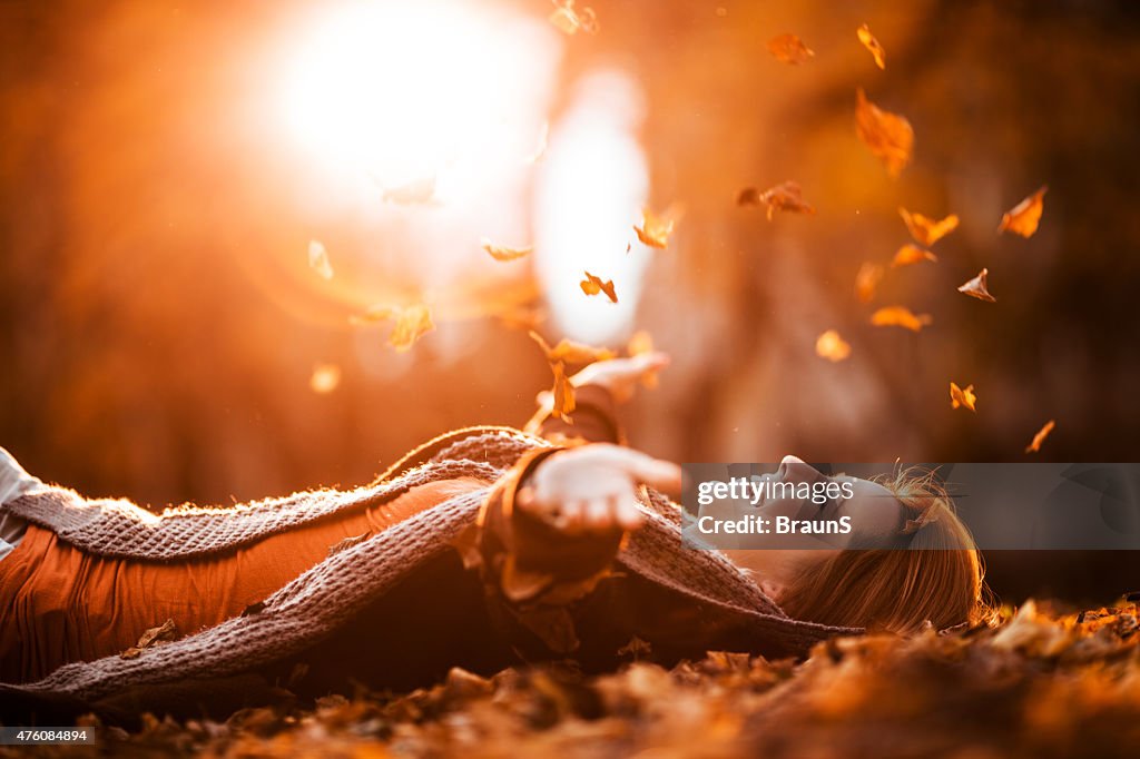 Carefree woman relaxing and throwing autumn leaves in nature.
