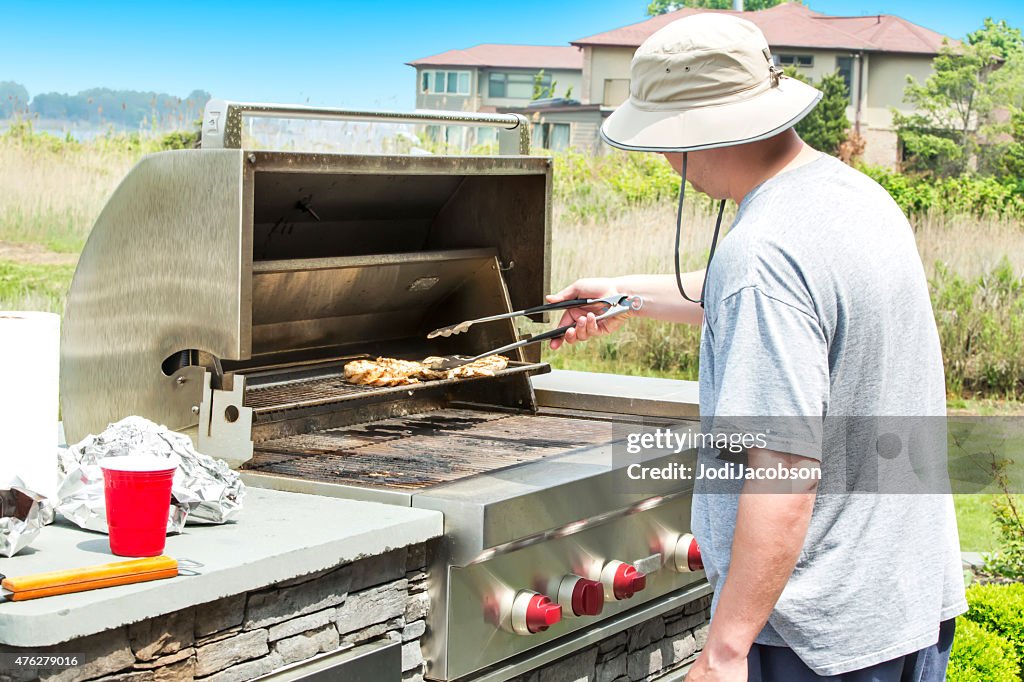 Man barbecuing chicken on a outdoor gas grill