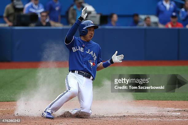Munenori Kawasaki of the Toronto Blue Jays slides across home plate to score a run on an RBI single by Jose Reyes in the ninth inning during MLB game...