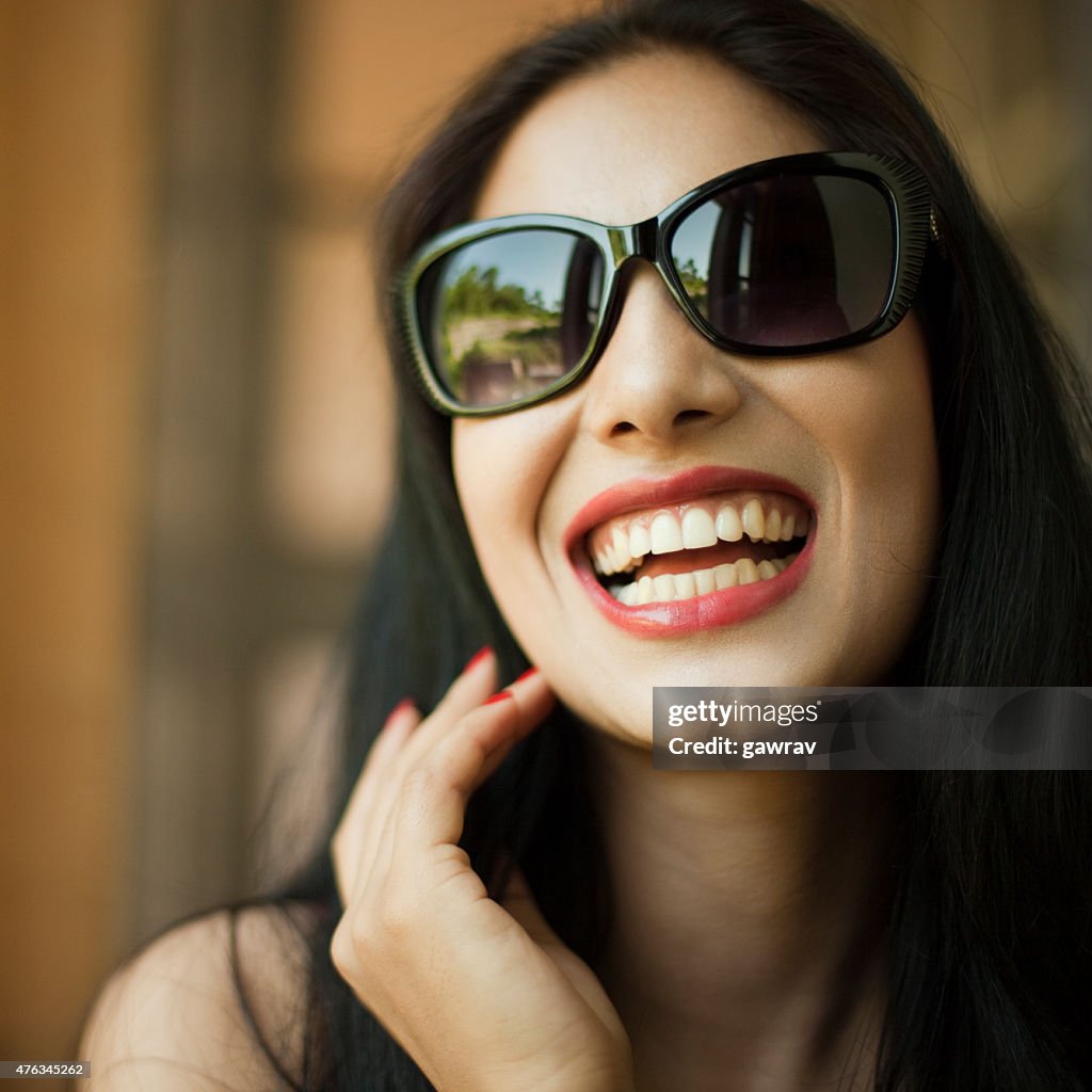 Belle jeune femme à lunettes de soleil rire à haute voix.