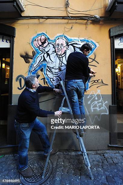 Bruno, the owner of the bar Nilo and one of his barmen attach on the wall a street art mural showing Pope Francis as a superman, flying through the...
