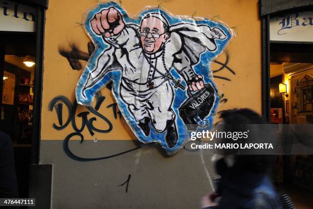 Woman looks at a street art mural showing Pope Francis as a superman, flying through the air with his white papal cloak billowing out behind him and...