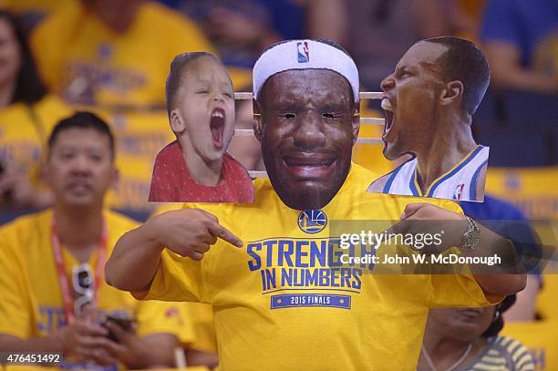 Finals: Golden State Warriors fan in stands wearing cardboard cutout of Cleveland Cavaliers LeBron James crying face along with Stephen Curry and...